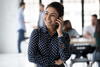 a woman smiles while talking on a phone with her arm crossed.